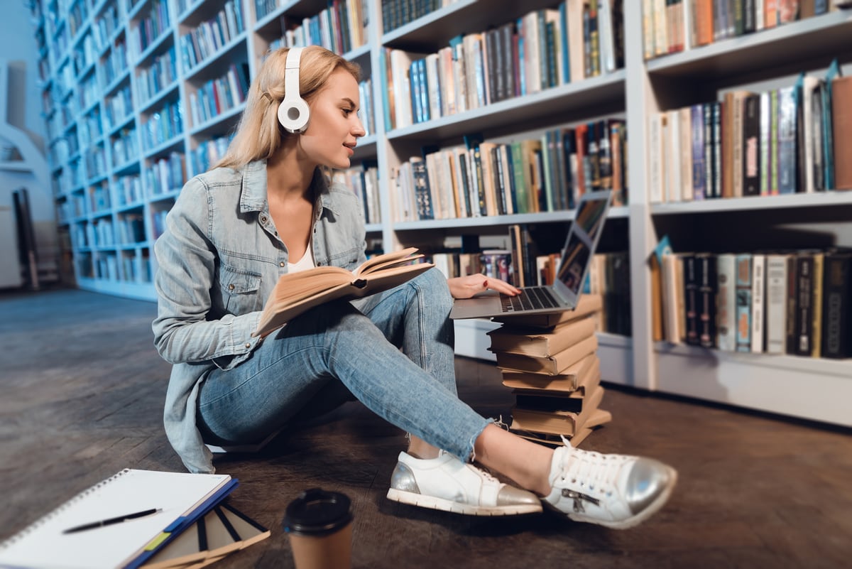 Bild einer Frau mit Kopfhörer vor einem Bücherschrank mit Laptop